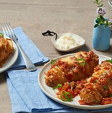 Eingeschnittene Kartoffeln mit Parmesan und Tomatensauce aus dem Ofen. Die Hasselback Kartoffeln werden mit Frühlingszwiebeln garniert und heiß serviert. 